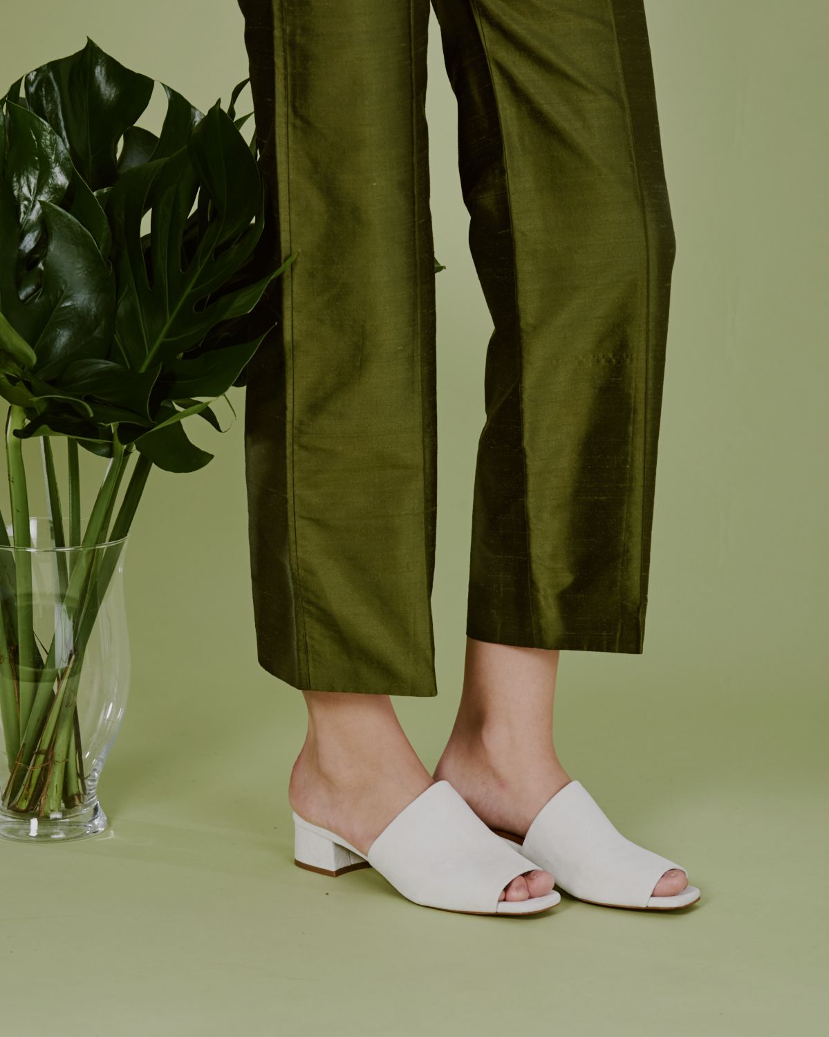 Model in green pants against green background in white slide on mules.