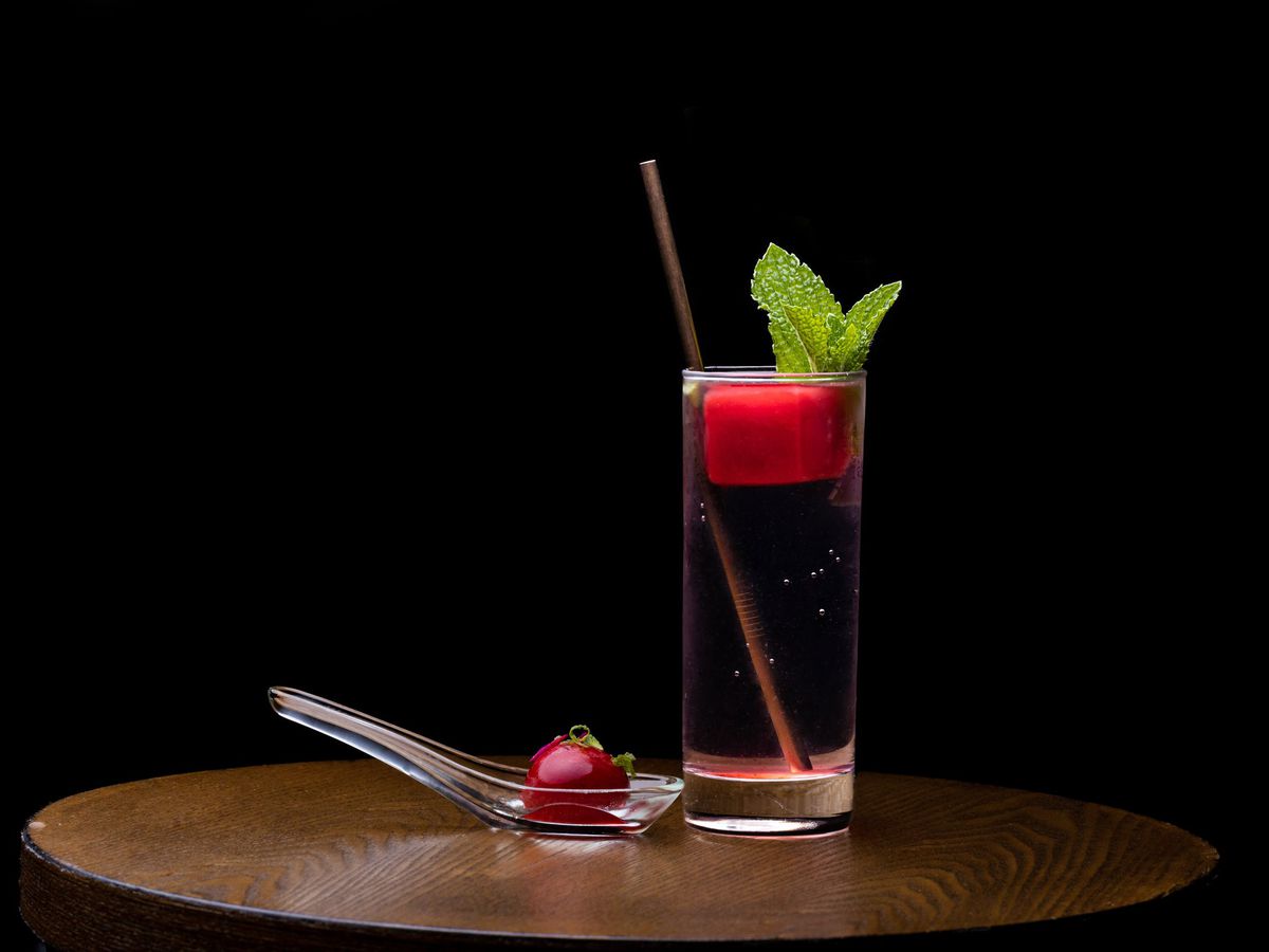 A cocktail glass with an opaque red ice cube floating at the top, garnished with mint. 