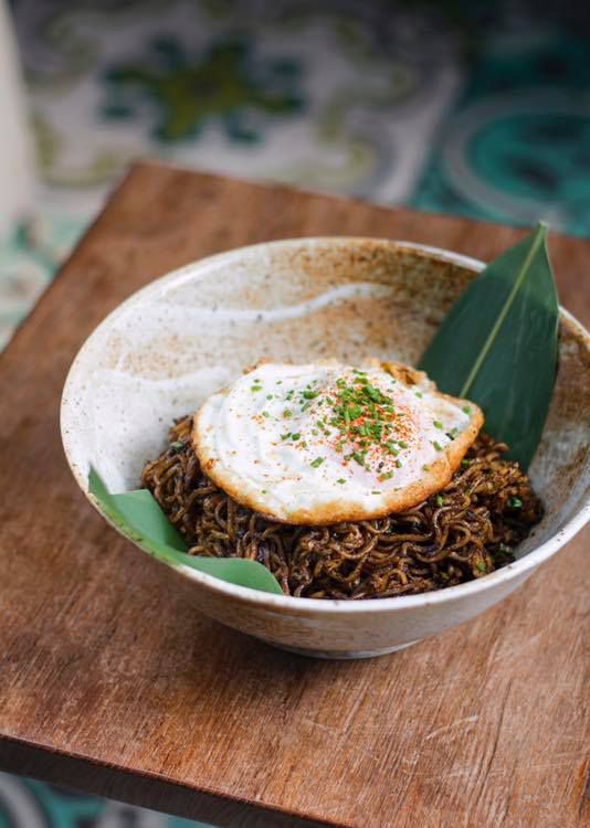 A bowl of maggie goreng, with an herb-dusted fried egg on top.