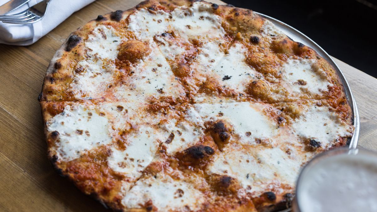 A charred sourdough pie is dotted with pools of white cheese.