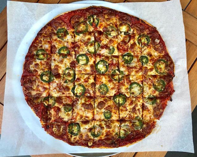 A pizza with jalapenos is on a sheet of parchment paper, cut into squares