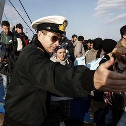 A Greek coast guard officer directs migrants and refugees after their arrival on a ferry at the port of Elefsina, west of Athens, on Sunday, March 20, 2016. Sunday is the day an agreement between the European Union and Turkey on ending illegal migration goes into effect — but its implementation still remains uncertain. Greek authorities say they're not sure any migrants entering Greece will be processed and turned back before Monday. 