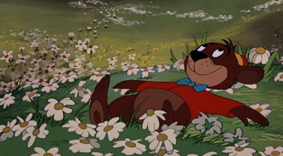 A cartoon bear in a red jacket and blue bow tie lies on his back in a field of daisies, smiling up at the sky, in Disney’s cartoon short “Bongo”