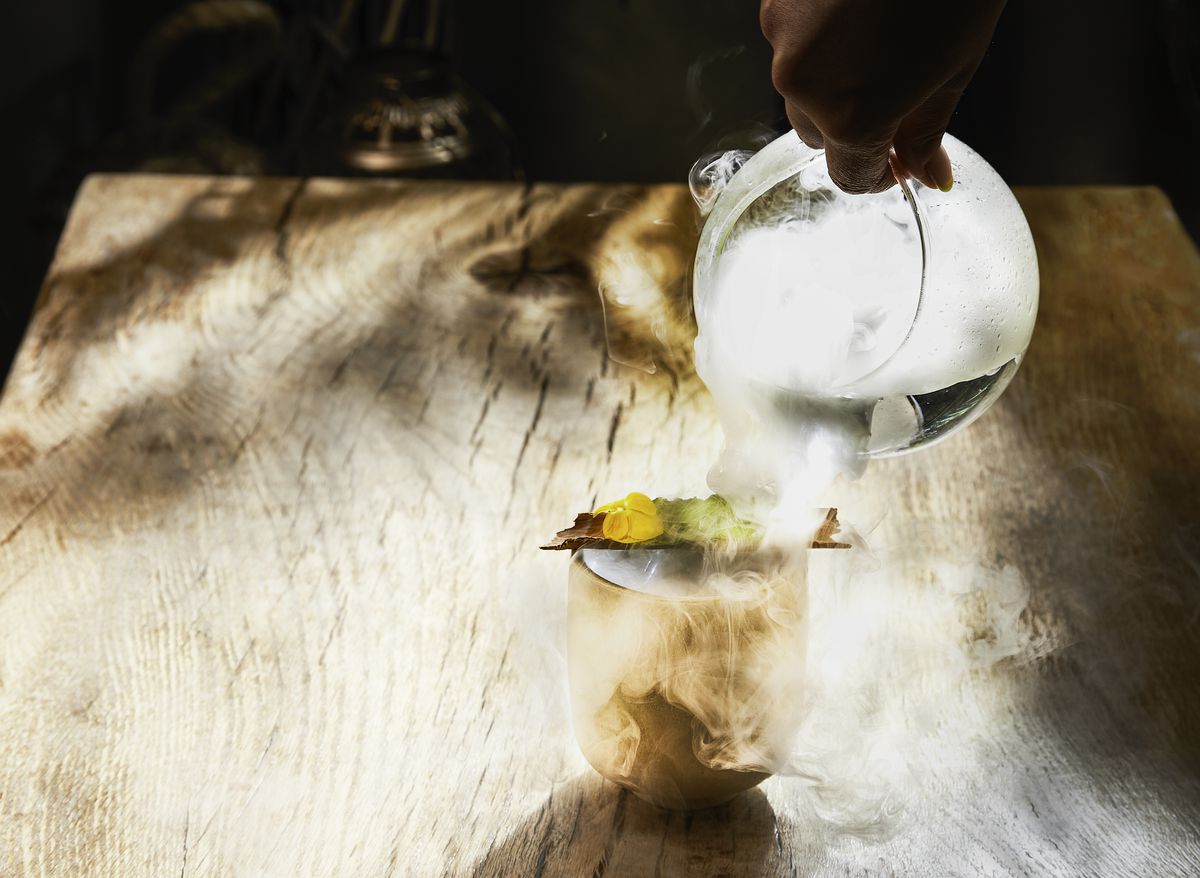A smoky cocktail poured into a clear glass on a wooden table.