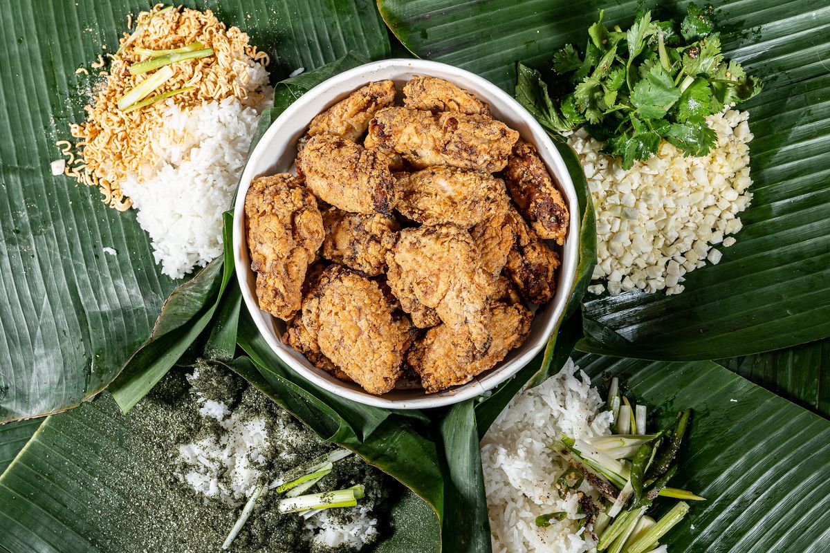 A bowl of fried chicken is surrounded by banana leaves, topped with rice, at Prey &amp; Tell