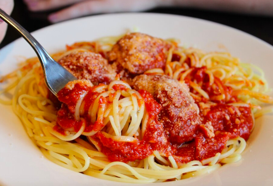 Closeup on a white plate of spaghetti and meatballs with a fork in it
