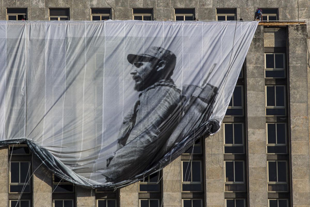 Men hang a giant banner with a picture of Cuba's late leader Fidel Castro as a young revolutionary, from the Cuban National Library building in Havana, Cuba, Sunday, Nov. 27, 2016. Cuba's government declared nine days of national mourning after Castro die