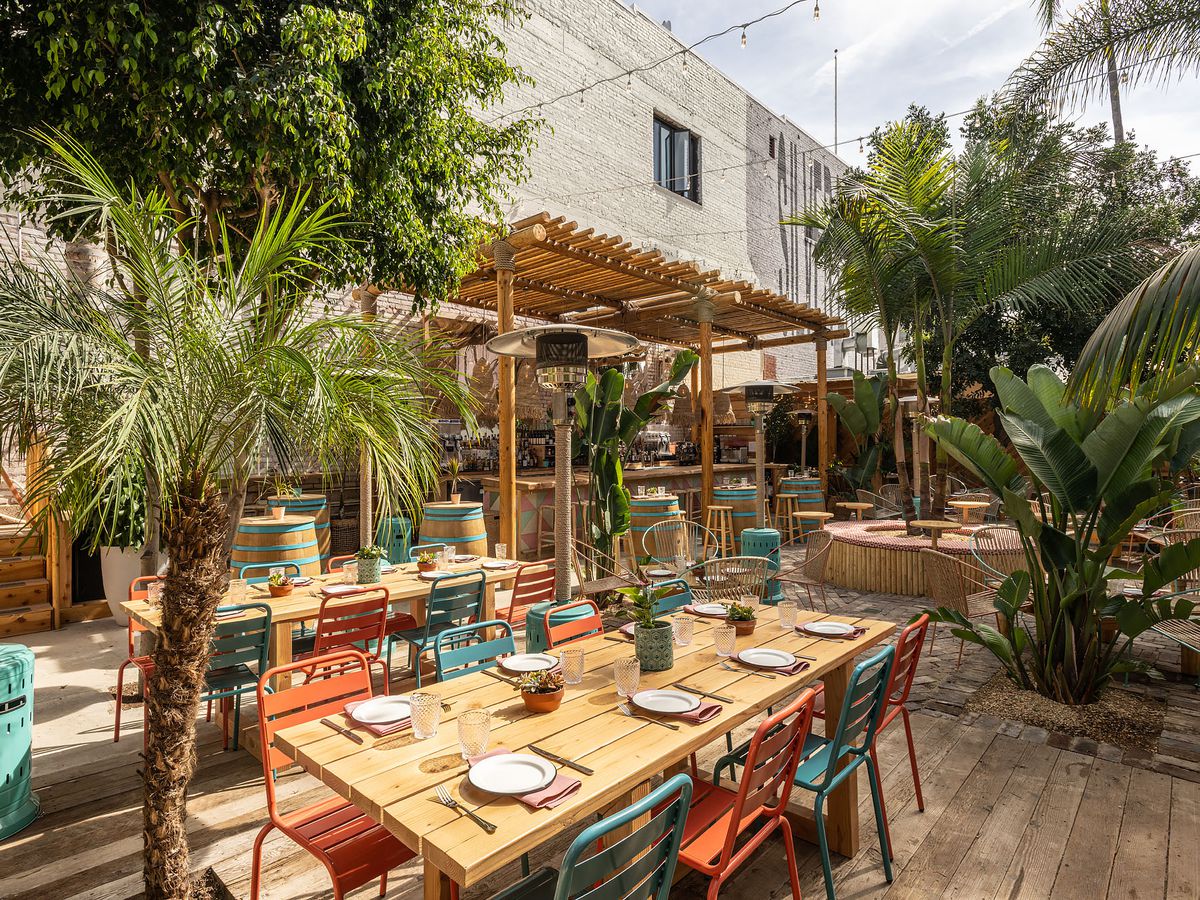 An outdoor patio with wood tables, colorful, planters, and a large bar with barstools.
