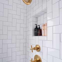 The shower’s herringbone tile wraps the new storage niches as well. The brushed-brass showerhead and controls were an easy swap in the existing locations. 