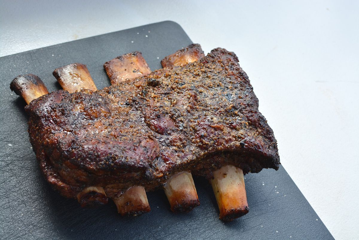 A set of beef ribs sit on a black cutting board.