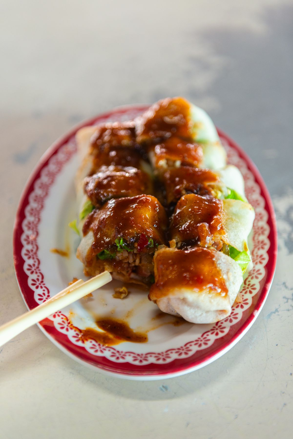 A spring roll topped with sauce and sliced, with chopsticks perched nearby.
