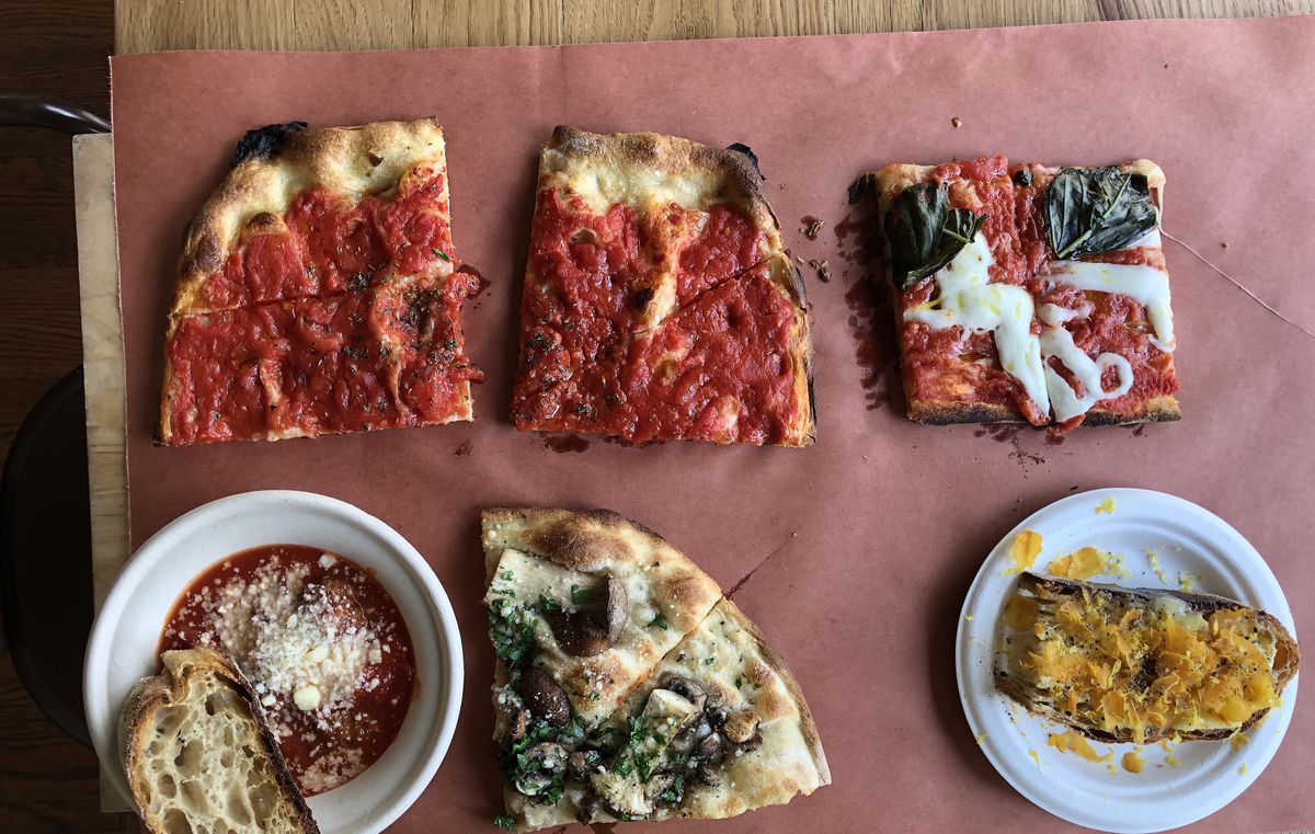 A spread of dishes, including tomato pizza, margherita pizza, meatballs, and bottarga toast, sits on a sheet of red butcher’s paper at Bread &amp; Salt in Jersey City