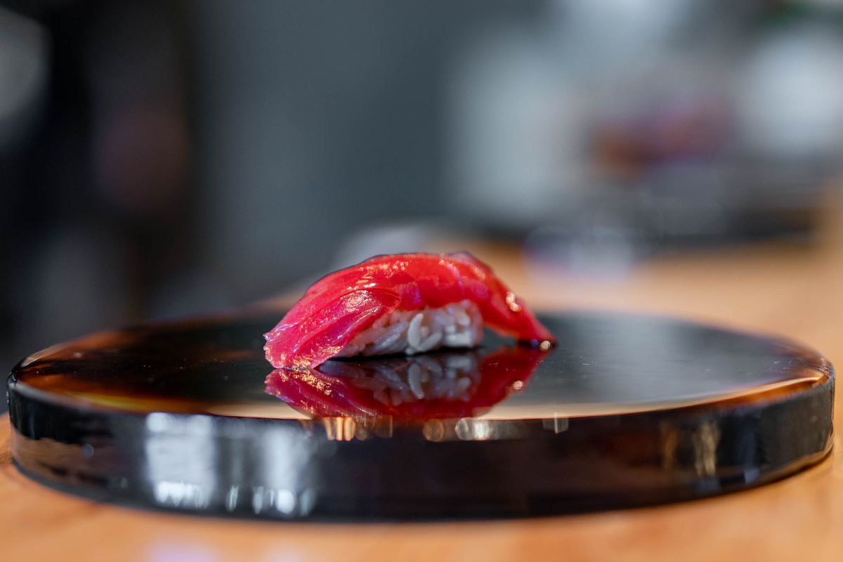 A dark red piece of fish nigiri on a black lacquered surface.
