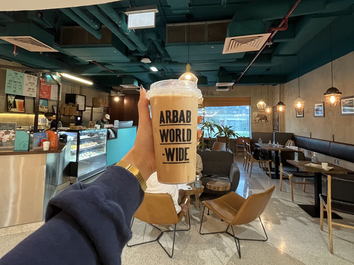 A hand holds up a plastic coffee cup branded with the words Arab World Wide