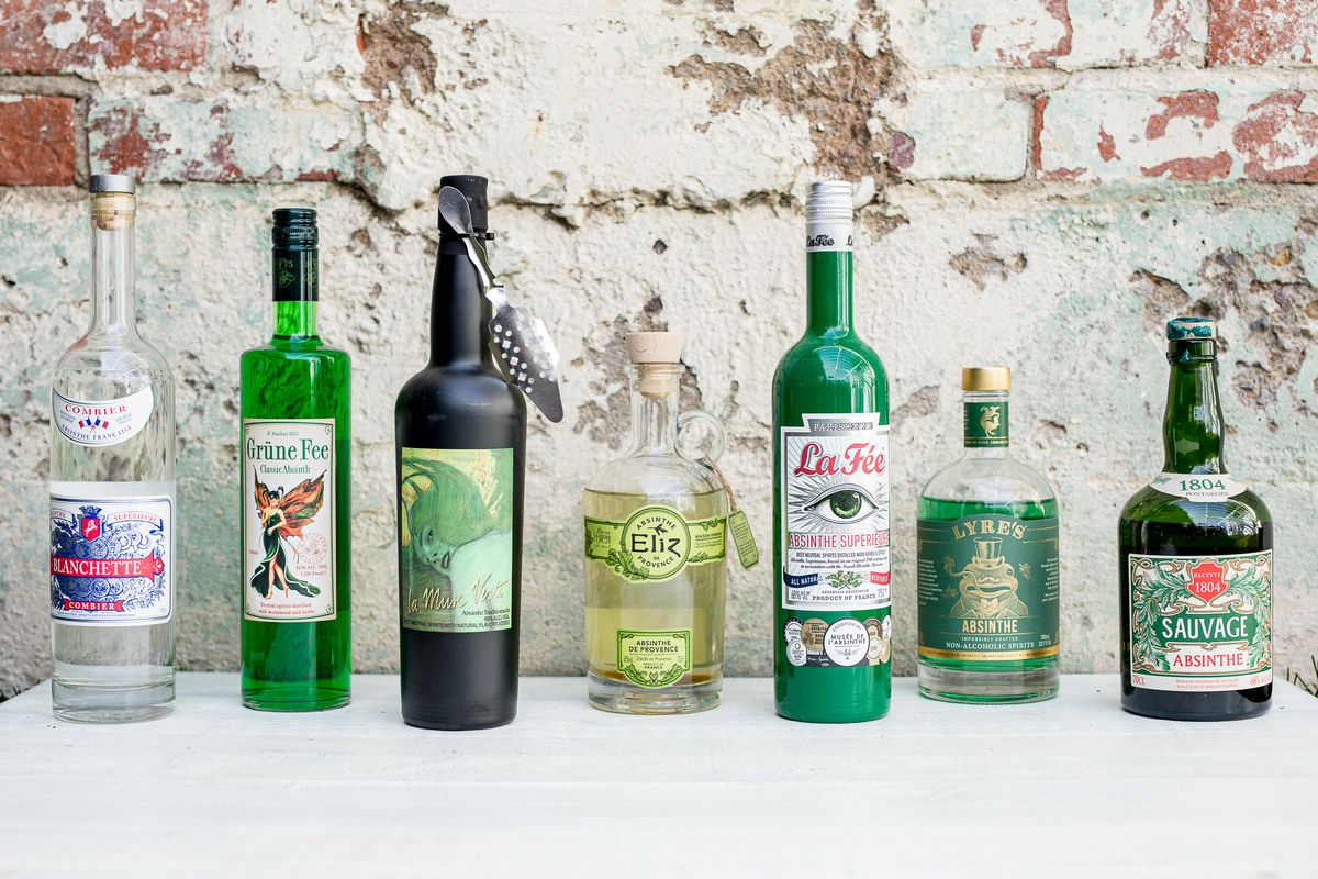 Seven different bottles of absinthe lined up on a table.