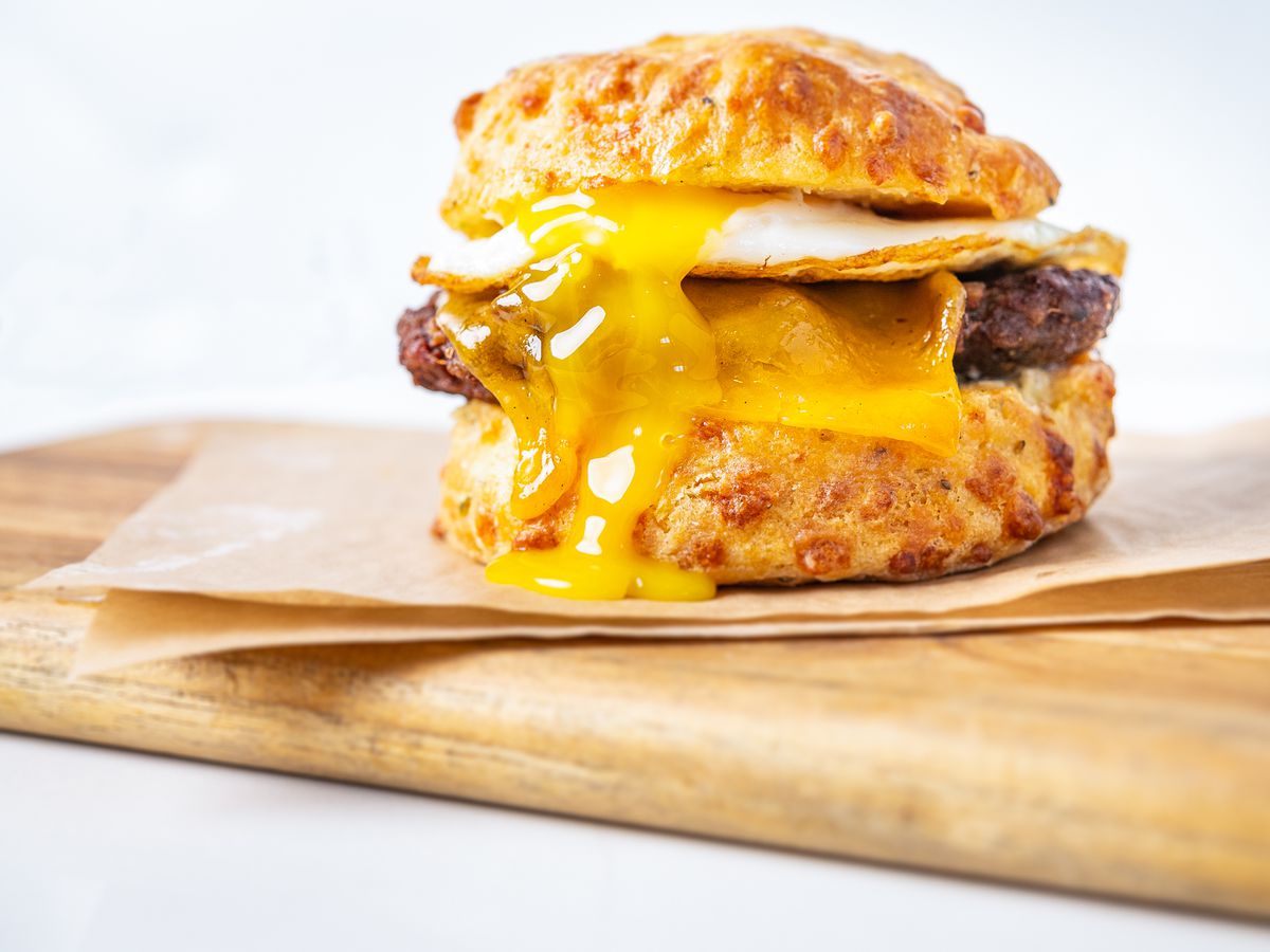 An egg sandwich with sausage oozes yolk onto a cheesy biscuit by Ghost Dog Egg Man