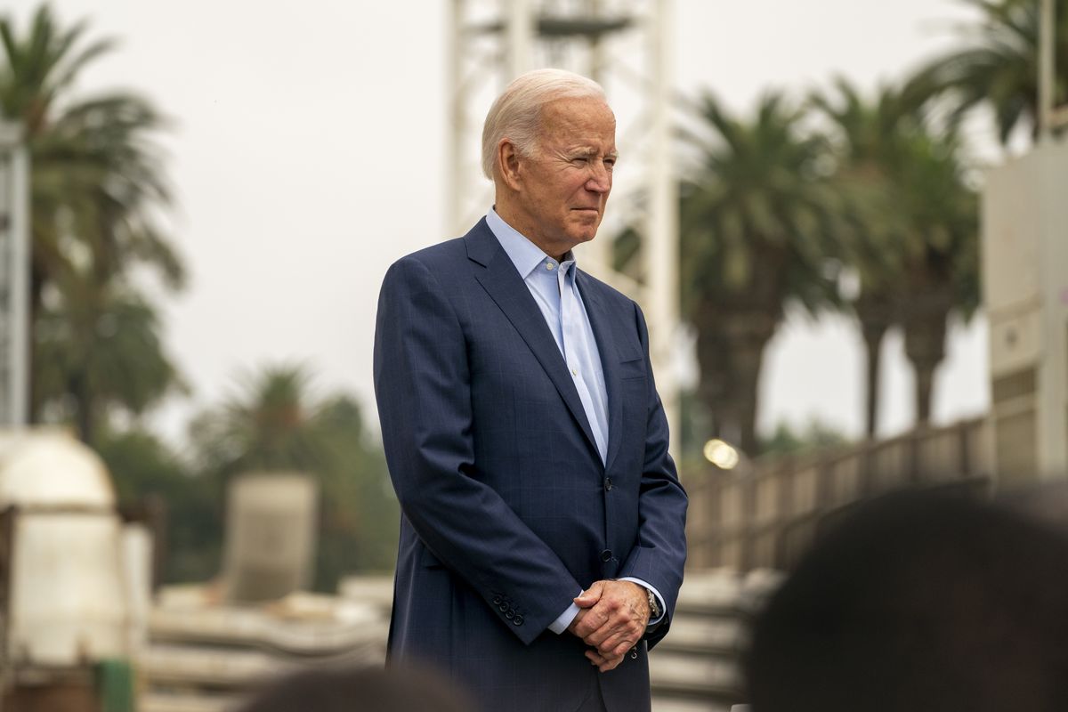 President Biden stands with his arms clasped in front of him. 