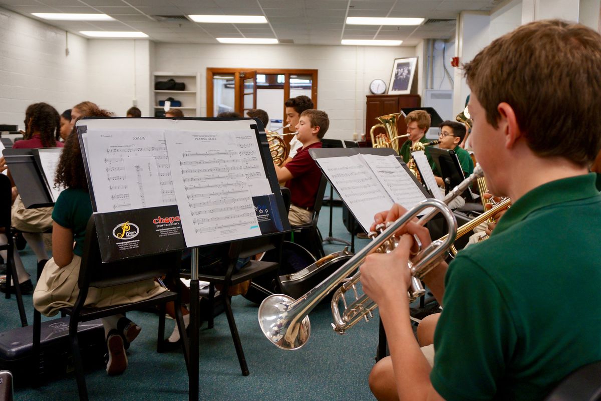 Middle school students practice the trumpet, tuba, French horn and other instruments in a classroom