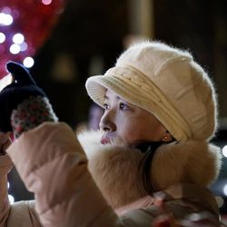 In this Dec. 14, 2016, photo, Jian Qing Chen, a recent arrival to New York from China's Fujian province, snaps a cell phone photo of Christmas decorations in the Dyker Heights neighborhood of the Brooklyn borough of New York. The area's elaborate, over-the-top Christmas displays on private homes draw thousands of visitors from all over the world. 
