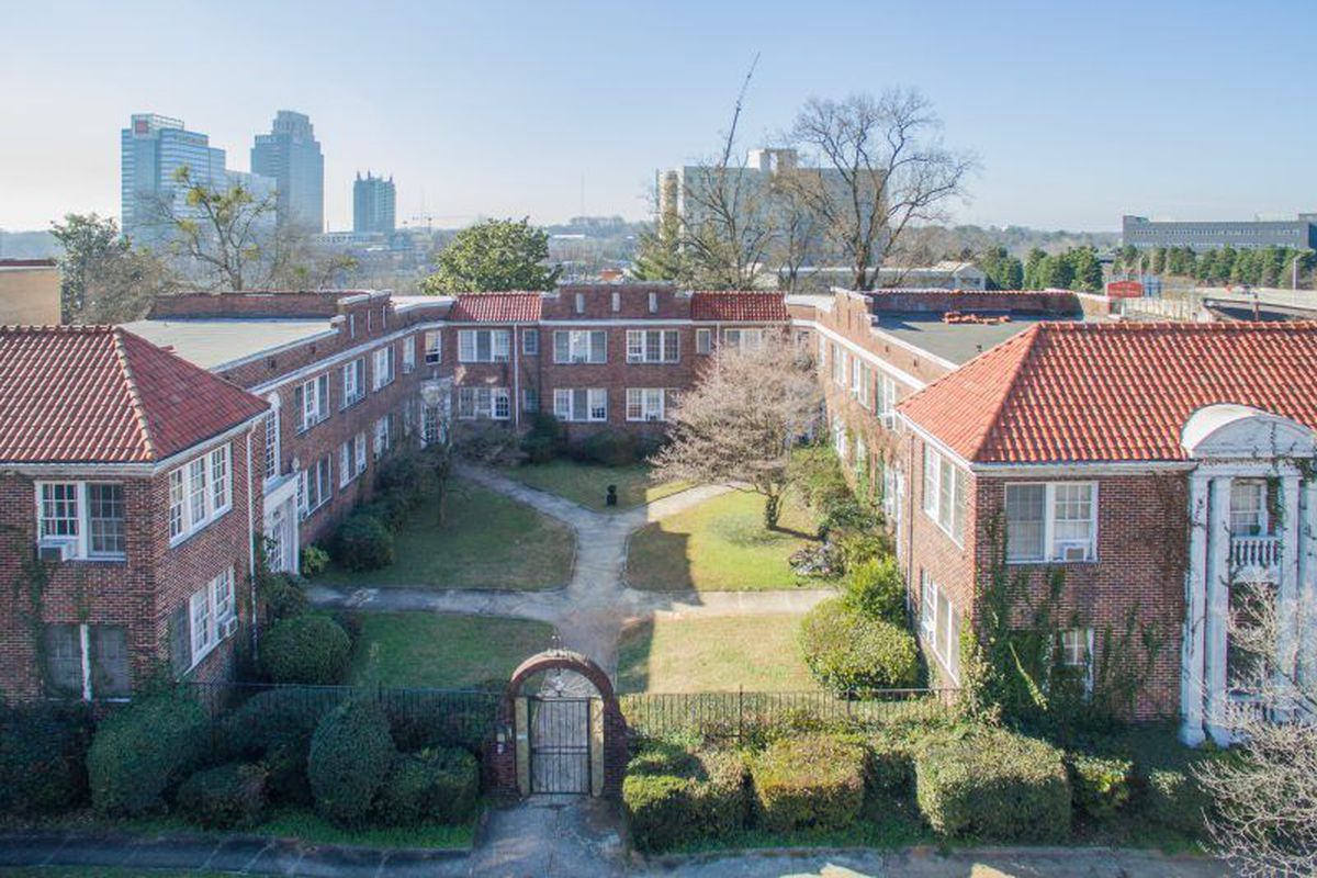 A low brick apartment building surrounding a courtyard with high-rises in the background.