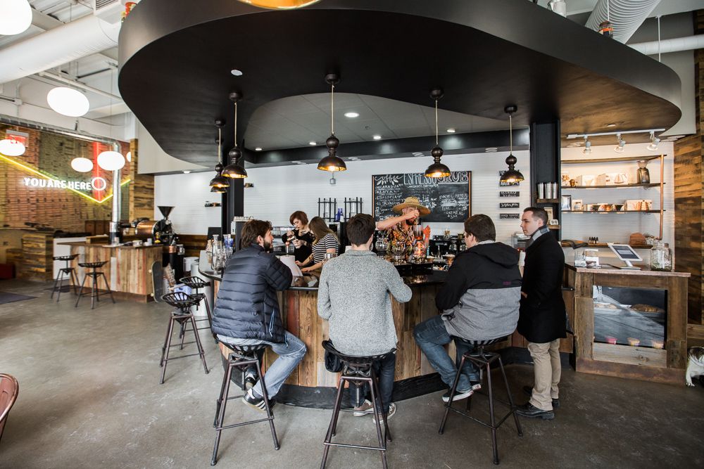 Customers in jackets and sweaters gather around a curved bar sitting at stools.