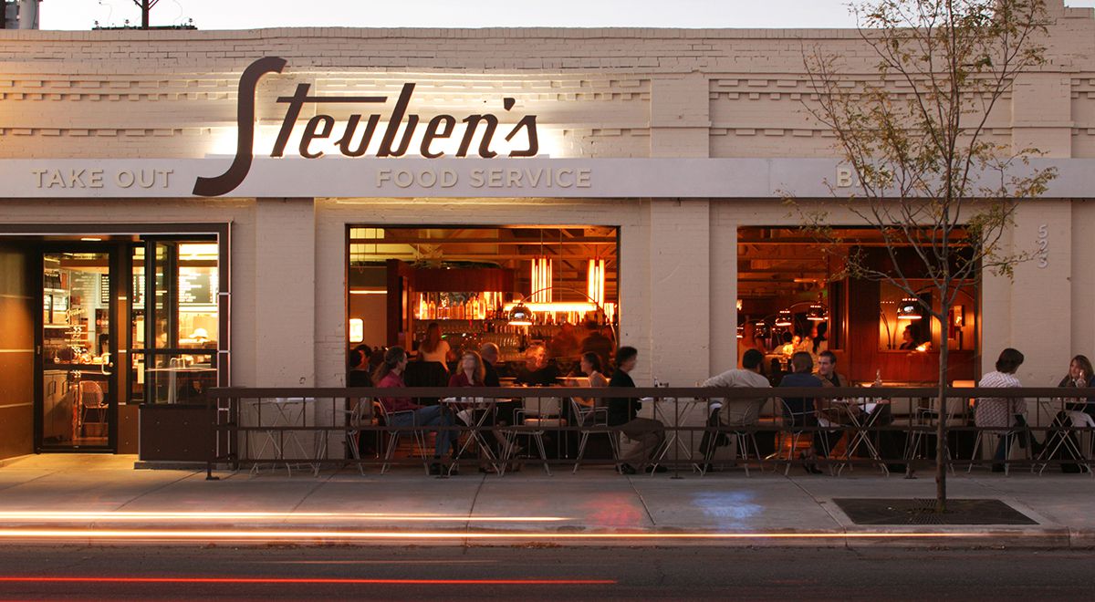 A photo of the exterior of Steuben’s showing the large Steuben’s sign and customers on the patio