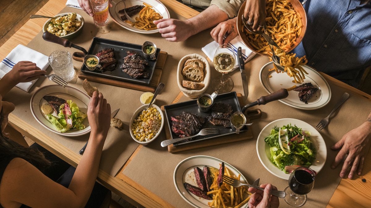 Four patrons dine on skirt steak and a variety of sides, as depicted in this overhead diagonal shot