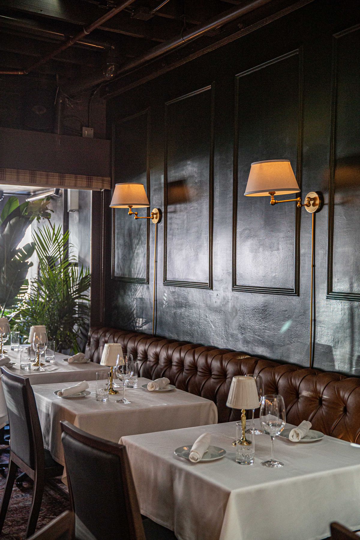 Dim lighting and dark walls at a new steakhouse with long banquette and table lamps.