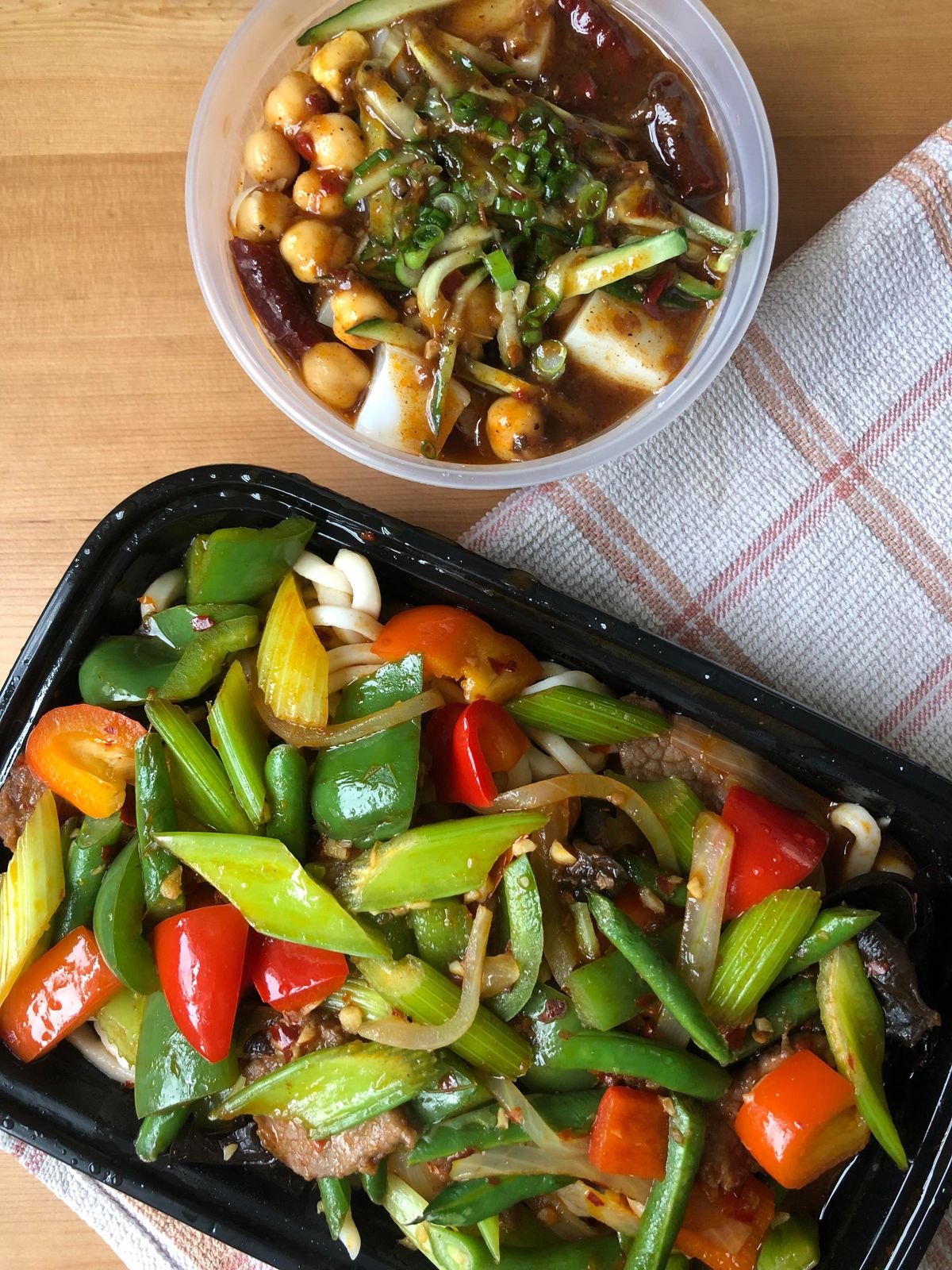 Two takeout containers, one filled with bean jelly and the other noodles and veggies including green and red peppers.