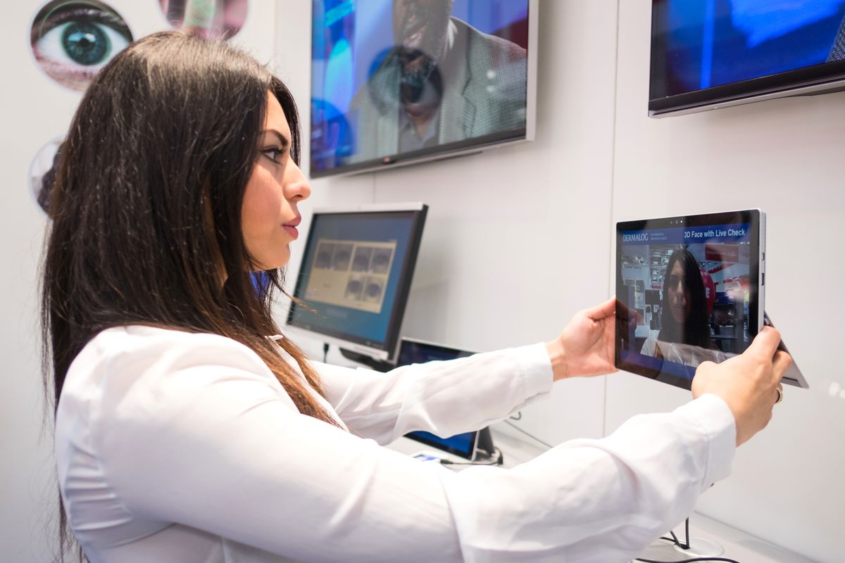 A woman holds a tablet featuring biometric 3D facial recognition software.