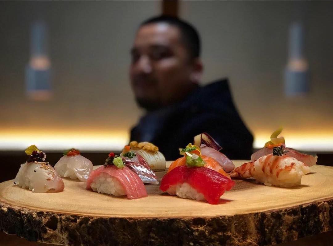 A man holding a wooden plate with rows of sushi.