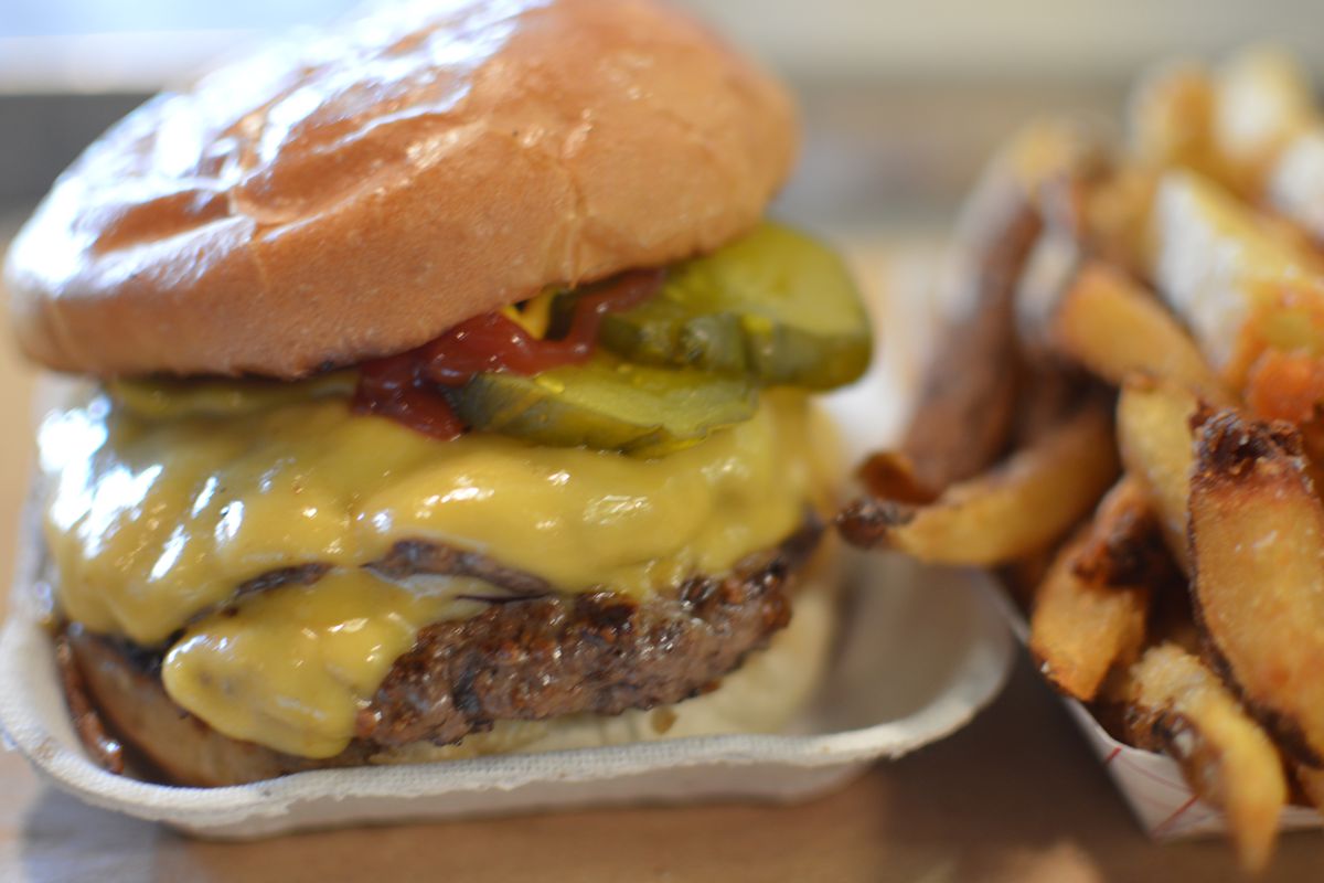A cheeseburger with two patties is topped with cheese, pickles, ketchup, and mustard, served with fries.
