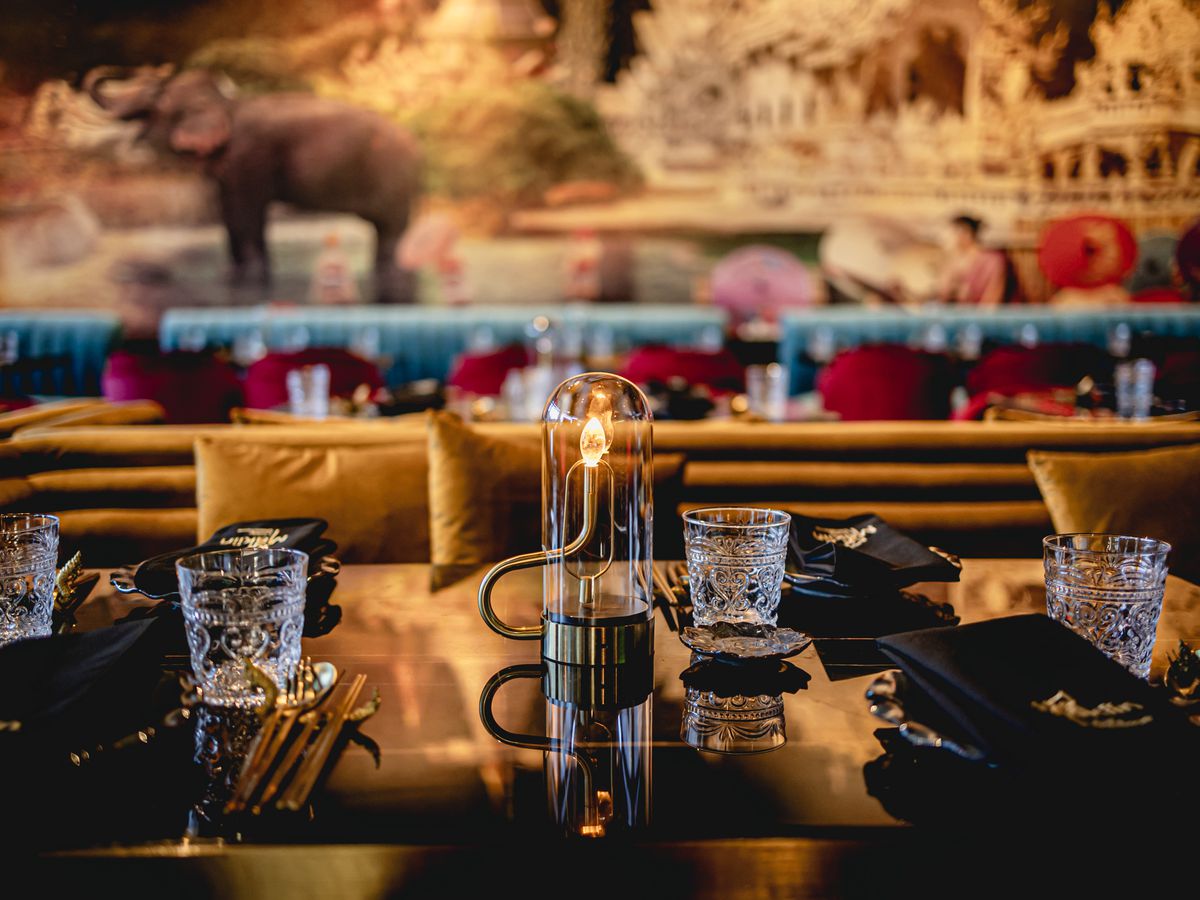A close-up of a golden dining table at MaKiin, topped with hand-crafted glasses and velvet booth seating.