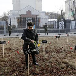 A woman places flowers on one of 30 crosses placed by activists bearing the names of people who died in shelling in Mariupol on Jan, 24, outside the Russian Embassy in Kiev, Ukraine, Sunday, Feb. 1, 2015. 