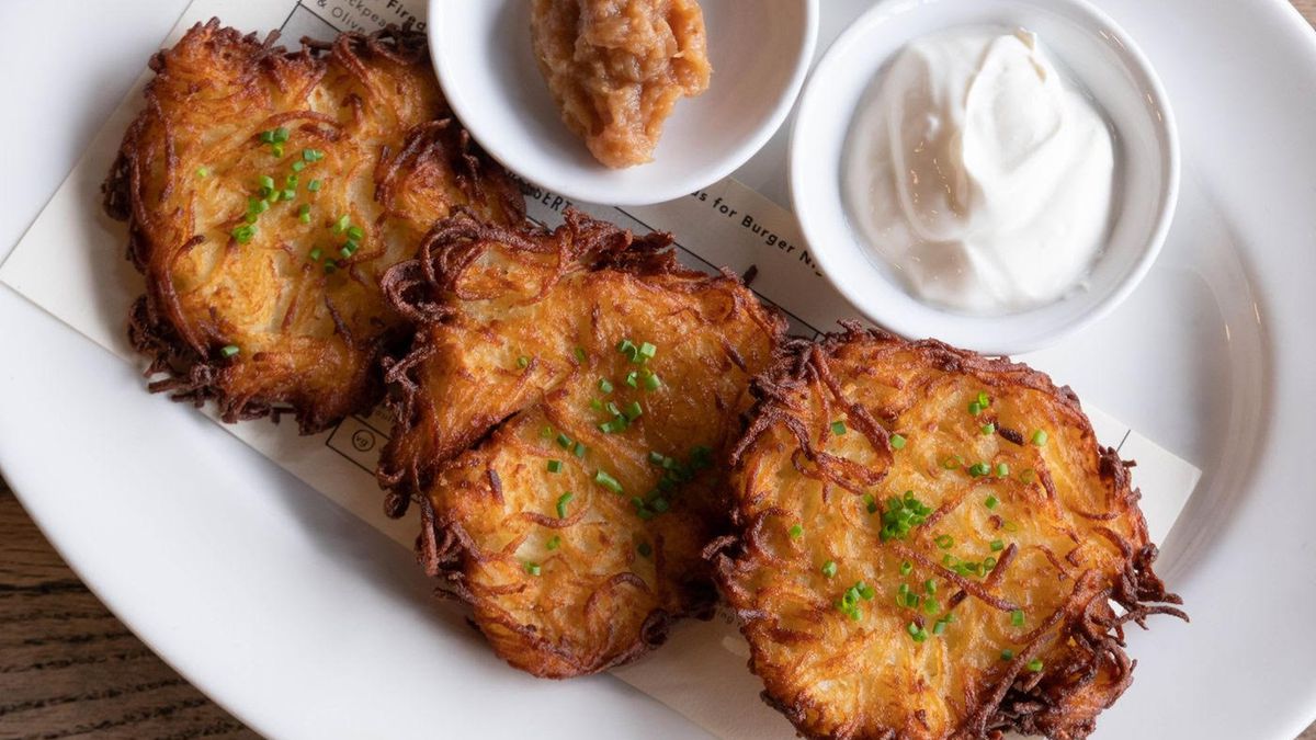 A white plate with three latkes on it and ramekins of apple butter and crème fraiche.