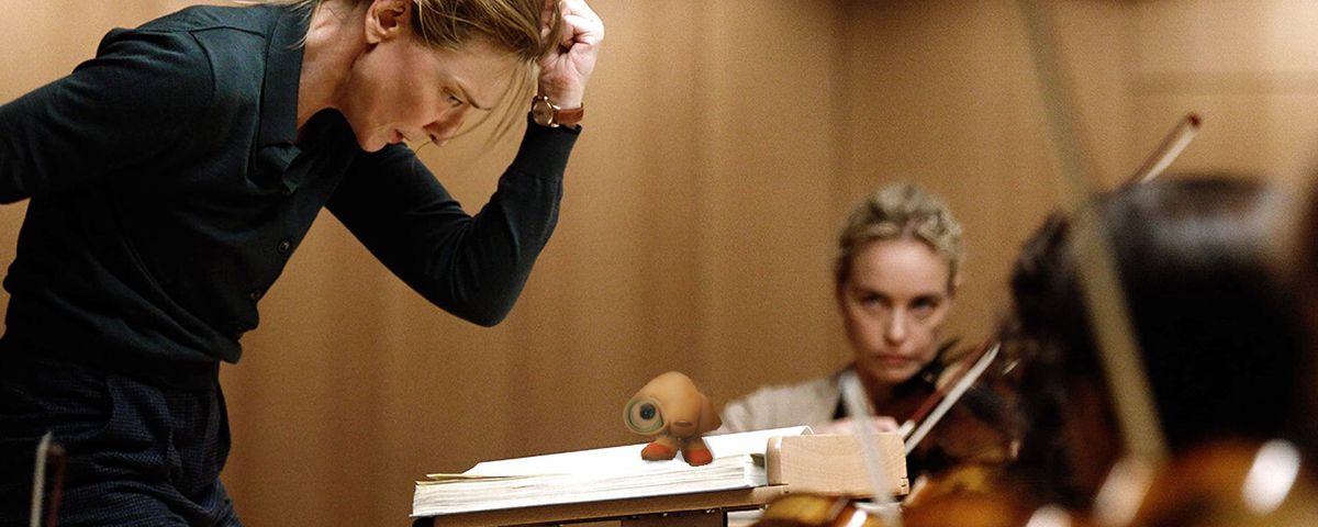 In a Photoshopped image, Lydia Tár (Cate Blanchett) conducts an orchestra with fierce gestures while Marcel, a small seashell in tennis shoes and googly eyes, sits by observing on her lectern