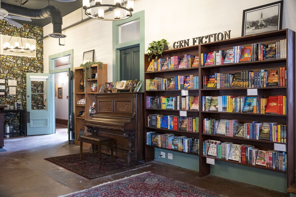 A wall of a bookstore with double-bookcases with books, and a wooden piano.