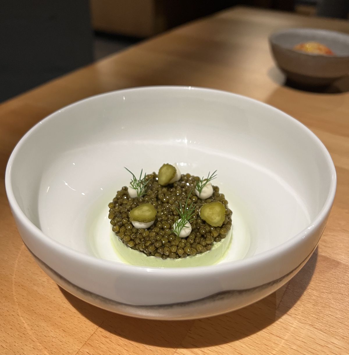 Golden osetra caviar sits atop light green dill mouse; dill fronds and sliced cornichons sit on top