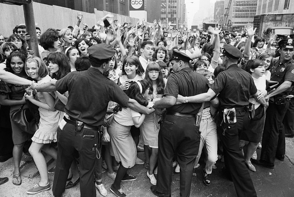 Uniformed police hold back a mob of fans.