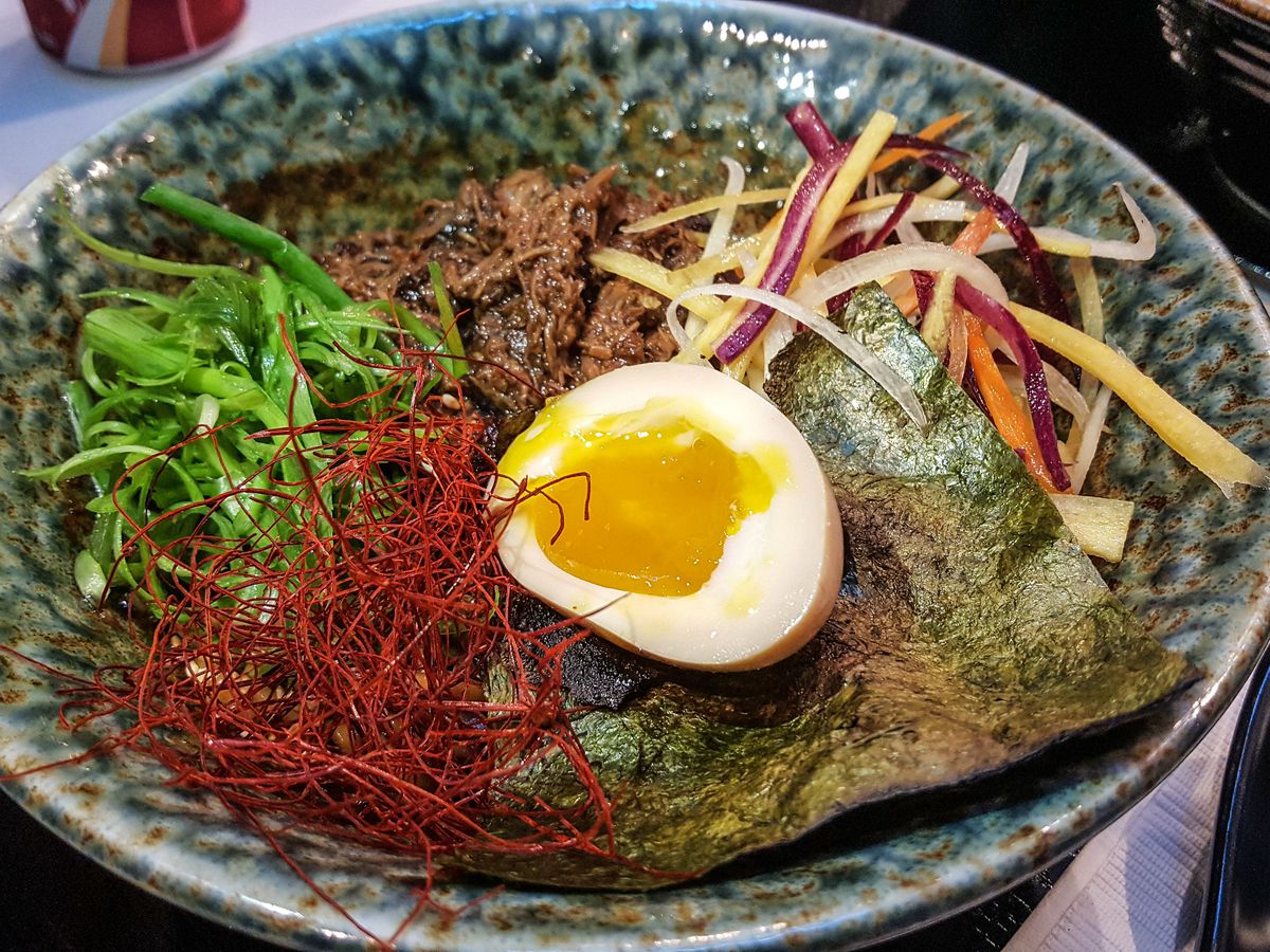 A bowl of ramen with saffron, a soft egg, seaweed, and chopped vegetables