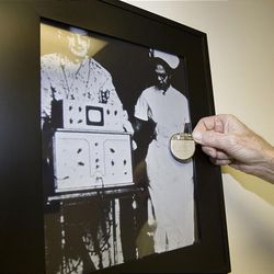 Dr. Olsen holds a modern pacemaker in front of a photo of one of the first pacemaker devices, which was almost as big as patients it treated.