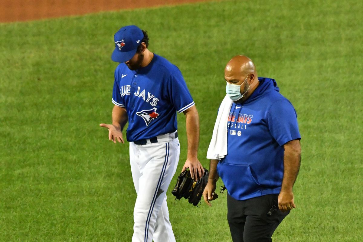 Toronto Blue Jays head trainer Jose Ministral (right) walks with relief pitcher Jordan Romano (left) who left the game after injuring his hand in the the 8th inning against the Baltimore Orioles at Sahlen Field.