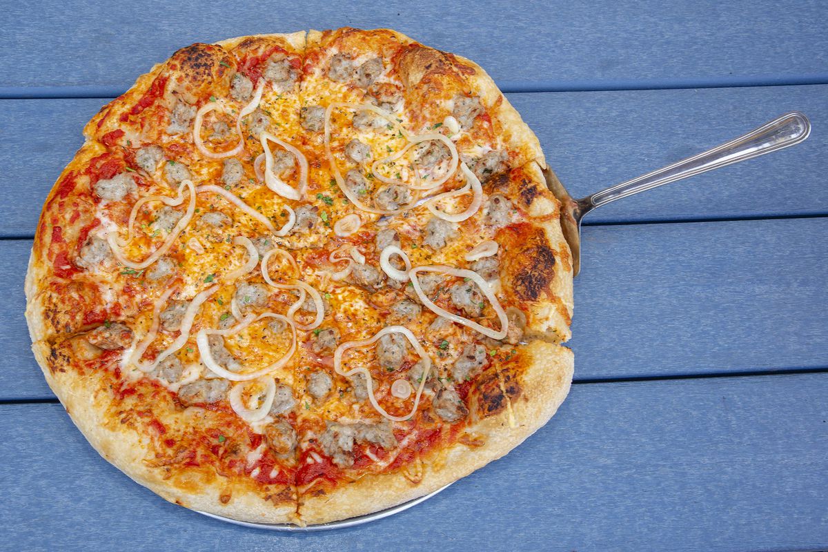 A sausage and onion pizza on a picnic table.