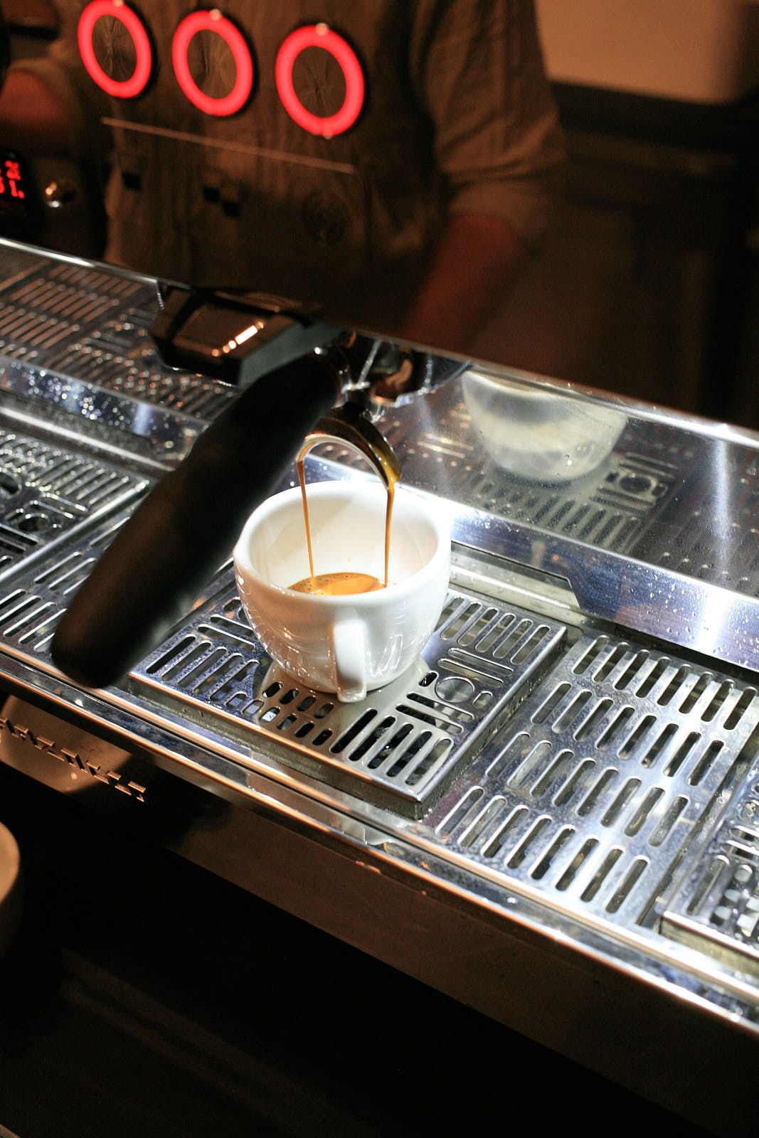 A shot of espresso flows out of a portafilter into a white ceramic cup.