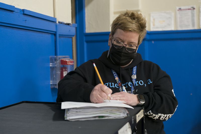 A school principal with short blonde hair works on documentation during a basketball game.