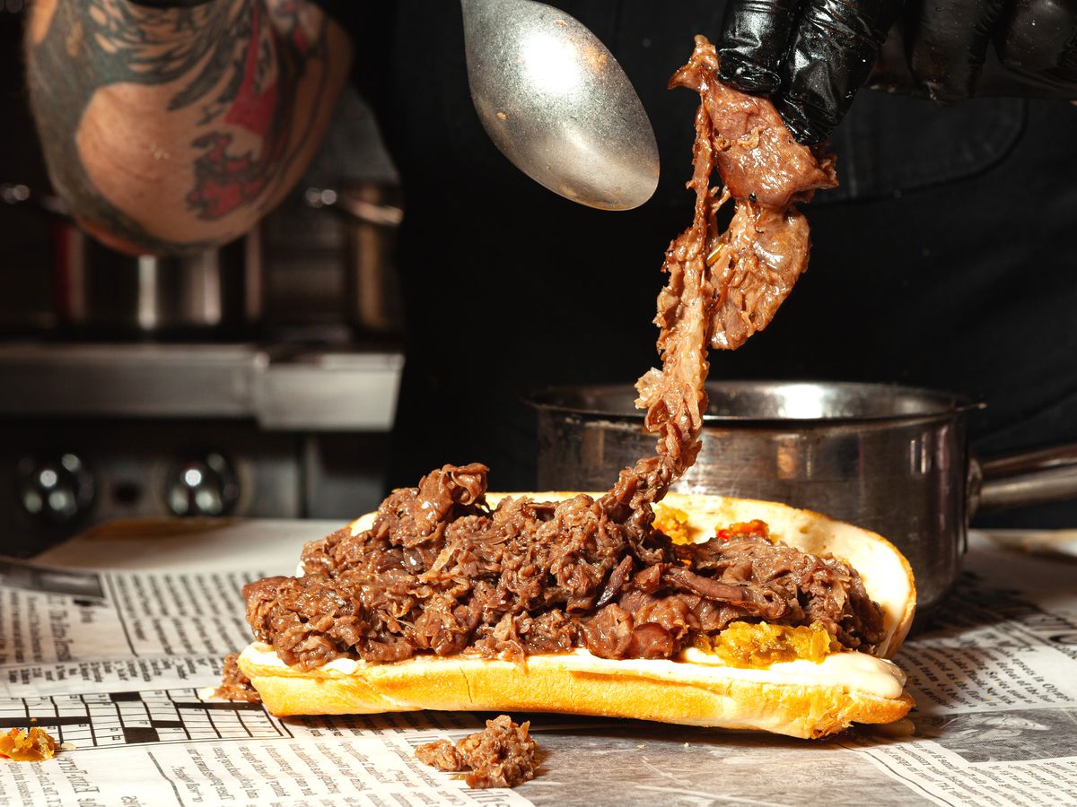 A chef piles shaved beef onto a sandwich roll.