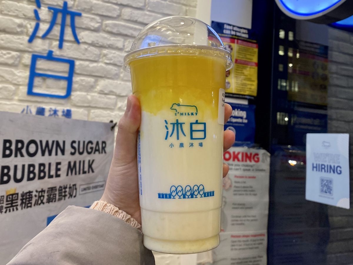 A yellow and white bubble tea is held up by a hand.