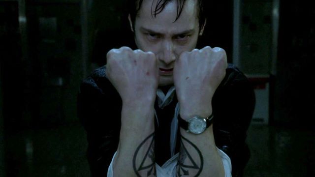 A wet Constantine holds up his two arms to form a rune tattoo
