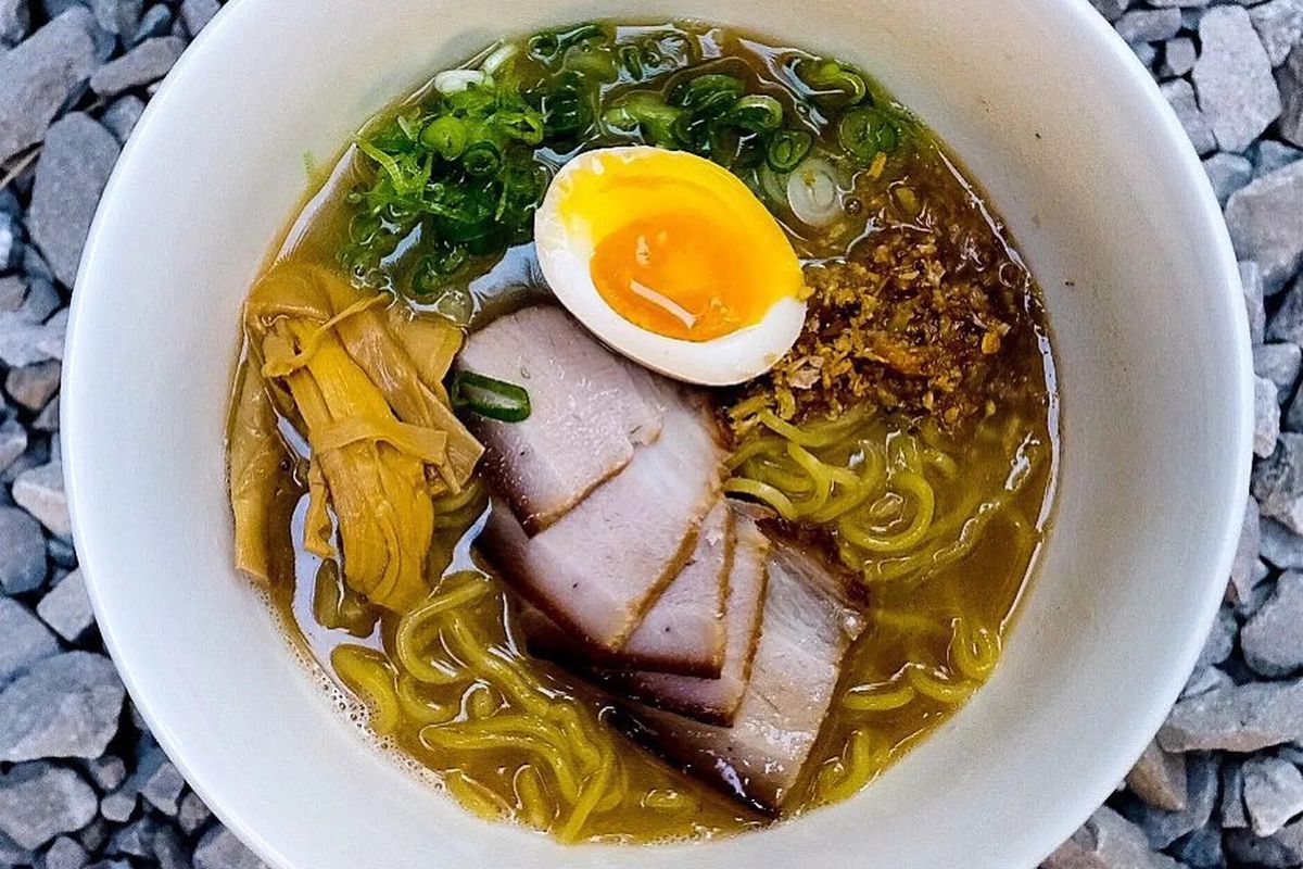 A bowl of Ramen with smoked chashu pork belly with bamboo shoots, scallions, fried garlic, and egg