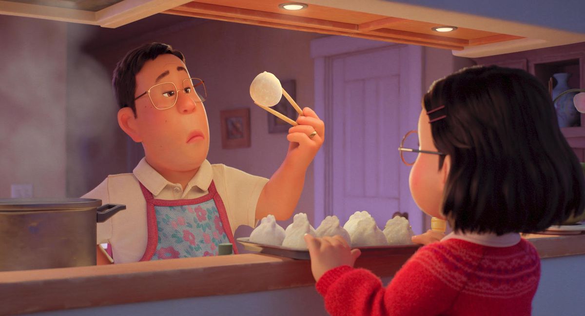 A still from Turning Red, in which a Chinese-Canadian man is looking at an uncooked bao he is holding with chopsticks, while his daughter faces him at the kitchen counter.